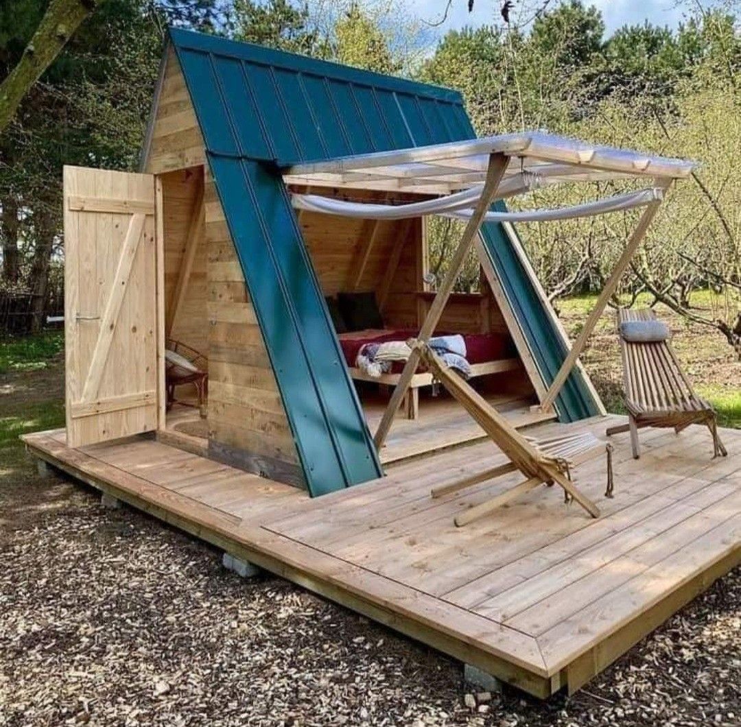 Mini chalé A-frame de madeira com telhado metálico verde sobre um deck de madeira